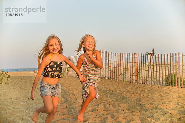 Porträt von blondhaarigen Schwestern  die Hand in Hand am Strand laufen.