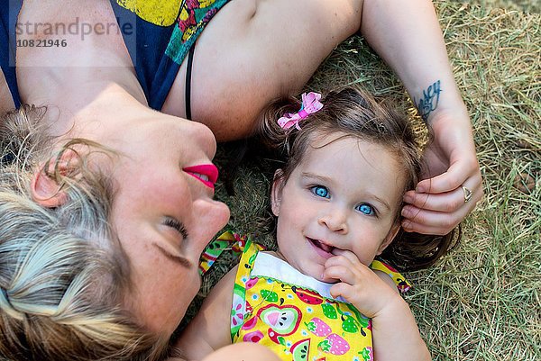 Overhead-Porträt einer mittelgroßen Frau und einer blauäugigen Kleinkind-Tochter  die auf Gras liegt.