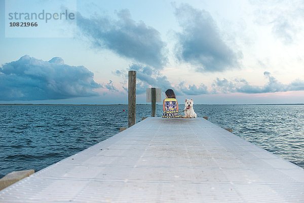 Porträt eines Hundes  der auf dem Pier neben dem Mädchen sitzt.