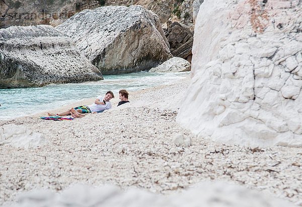 Junge Männer entspannen am felsigen Strand mit dem Smartphone  Golfo di Orosei  Sardinien  Italien