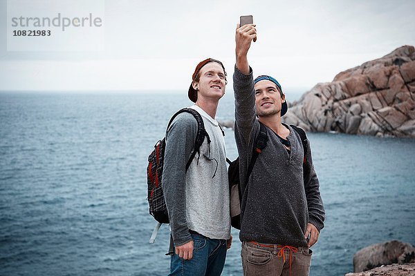 Junge Männer vor dem Meer mit dem Smartphone  um Selfie lächelnd zu nehmen  Costa Smeralda  Sardinien  Italien