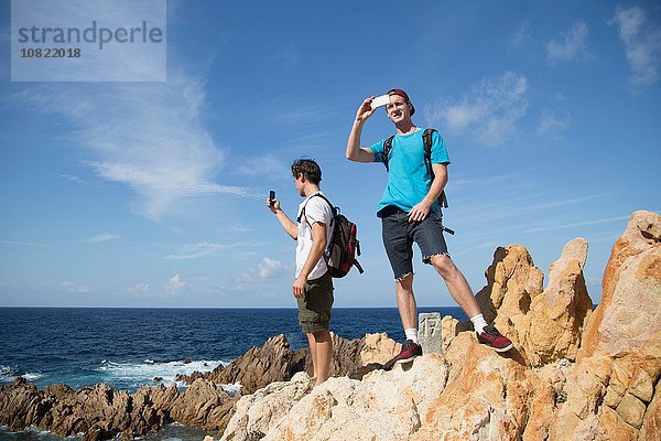 Junge Männer auf Felsen stehend mit dem Smartphone fotografieren  Costa Paradiso  Sardinien  Italien