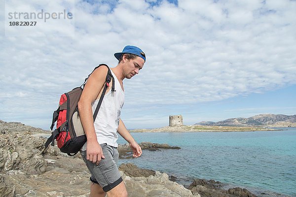 Junger Mann auf Felsen am Meer mit Rucksack mit Blick nach unten  Stintino  Sardinien  Italien