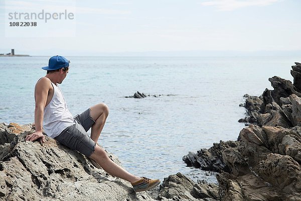 Seitenansicht des jungen Mannes auf Felsen mit Blick aufs Meer  Stintino  Sardinien  Italien
