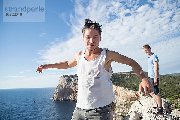 Junger Mann mit Weste auf Klippe am Meer in offenen Armen in Springhaltung  Capo Caccia  Sardinien  Italien
