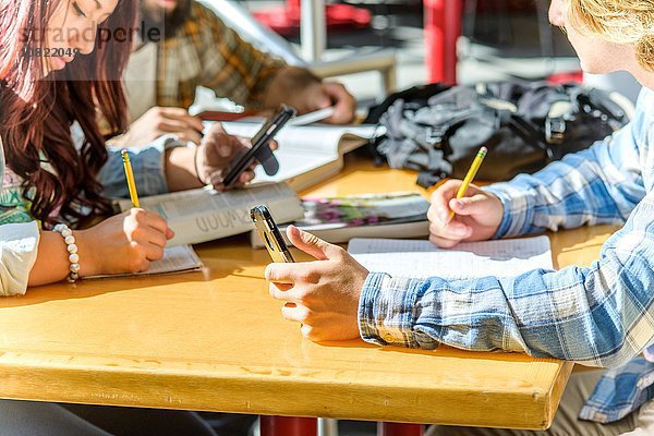 Ausschnittaufnahme von Studenten mit Smartphones und Schreiben am Schreibtisch