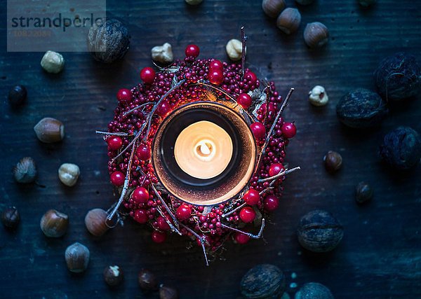 Draufsicht auf die brennende Kerze mit Beerenkranz und Nüssen
