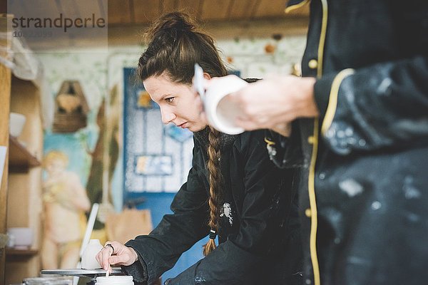 Seitenansicht der jungen Frau in der Werkstatt beim Rühren der keramischen Glasur  wegblickend