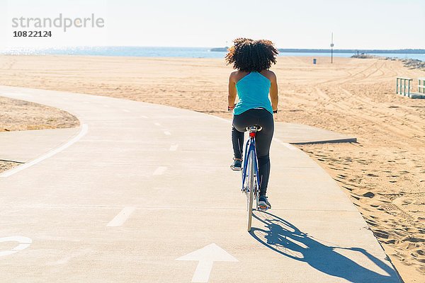 Mittlere erwachsene Frau auf dem Radweg am Strand  Rückansicht