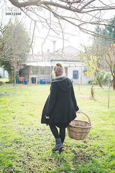 Durchgehende Rückansicht der jungen Frau im Garten mit Weidenkorb