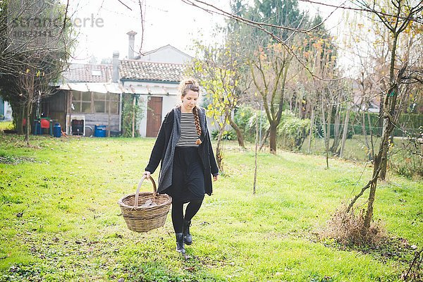 Durchgehende Vorderansicht der jungen Frau im Garten mit Weidenkorb