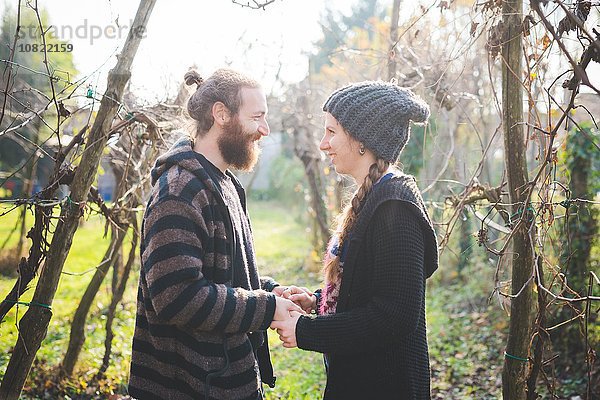 Seitenansicht des Paares zwischen den Bäumen von Angesicht zu Angesicht  Händchen haltend  lächelnd