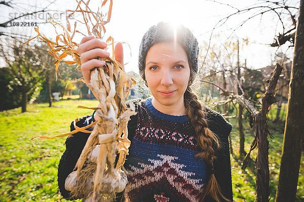 Junge Frau im Garten mit frisch gepflückten Knoblauchzwiebeln und lächelndem Blick auf die Kamera