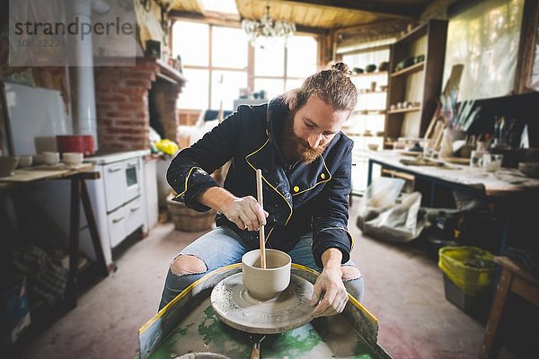 Der bärtige erwachsene Mann in der Werkstatt sitzend an der Töpferscheibe mit Hilfe eines Diddlers  um Tontopf herzustellen