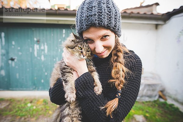 Junge Frau mit Strickmütze kuschelnde Katze  Blick auf die Kamera lächelnd