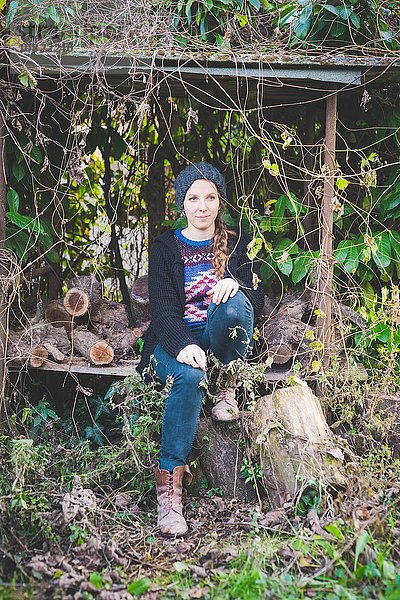 Junge Frau mit Strickmütze im Holzlagerhaus sitzend und wegschauend