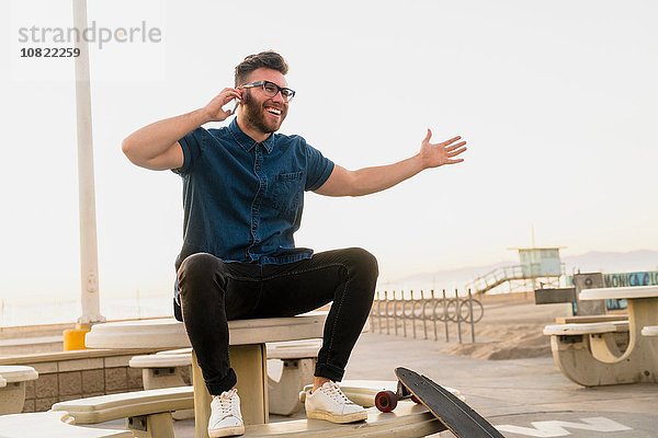 Junger Mann im Freien sitzend  mit Smartphone  lachend