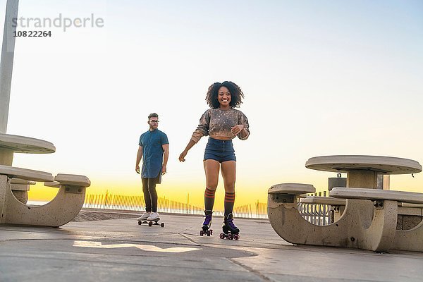 Junger Mann auf dem Skateboard  folgende erwachsene Frau auf Rollschuhen