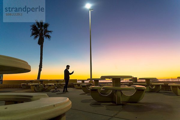 Junger Mann  draußen bei Sonnenuntergang  mit Smartphone