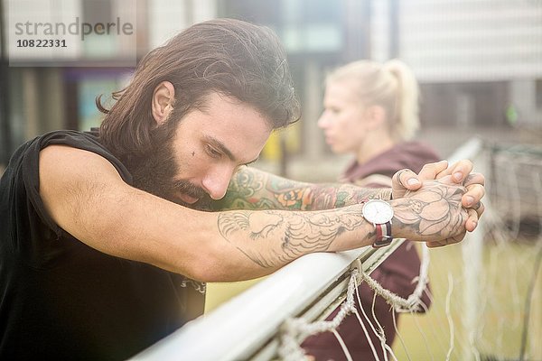 Mittlerer Erwachsener  der eine Pause einlegt und sich auf ein Fußballtor stützt.