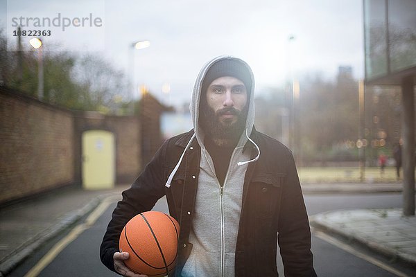 Porträt eines erwachsenen Mannes in der Straße  der Basketball hält.