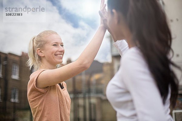 Zwei junge Frauen geben High Five  draußen.