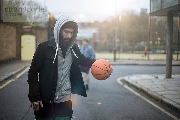 Ein erwachsener Mann  der die Straße entlang läuft und Basketball spielt.