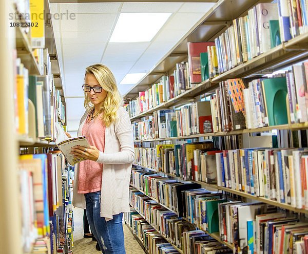 Junge Frau liest Buch aus Bibliotheksregalen