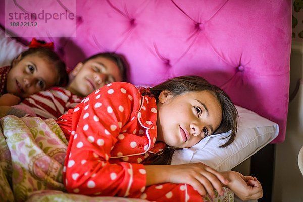 Junge und zwei Schwestern  die vor dem Schlafengehen im Bett liegen.