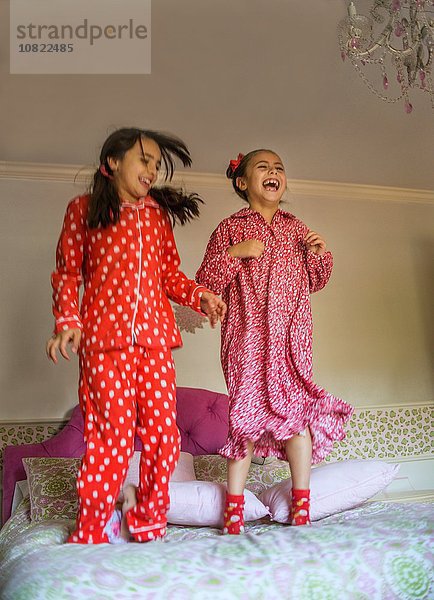 Zwei glückliche Schwestern springen auf dem Bett.