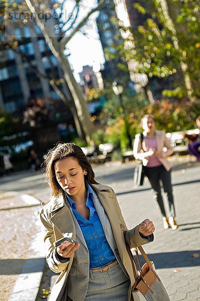Junge Frau liest Smartphone beim Spaziergang durch den Stadtpark