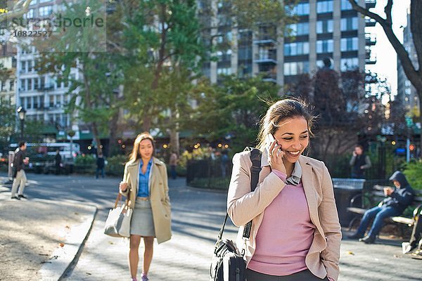 Junge Frau beim Spaziergang durch den Stadtpark am Smartphone