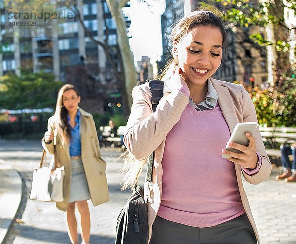 Junge Frau liest Smartphone-Texte beim Spaziergang durch den Stadtpark