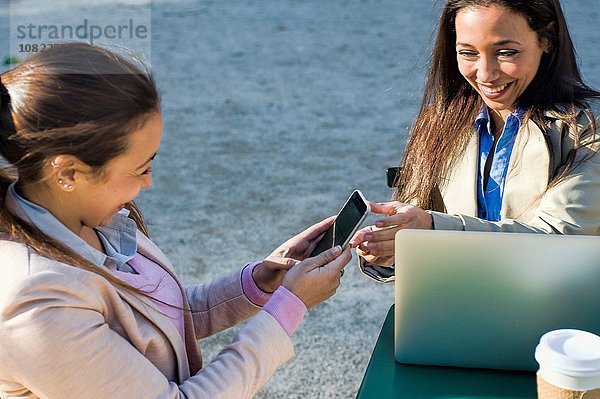 Junge erwachsene Zwillinge mit Laptop und Smartphone im Straßencafé