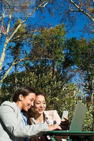 Junge erwachsene Zwillinge mit Laptop und Smartphone im Stadtpark