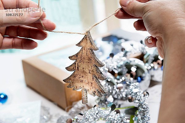 Personenhände beim Vorbereiten von Weihnachtsdekoration in Form eines Holzbaums