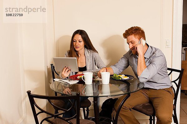 Paar am Esstisch mit Smartphone und digitalem Tablett