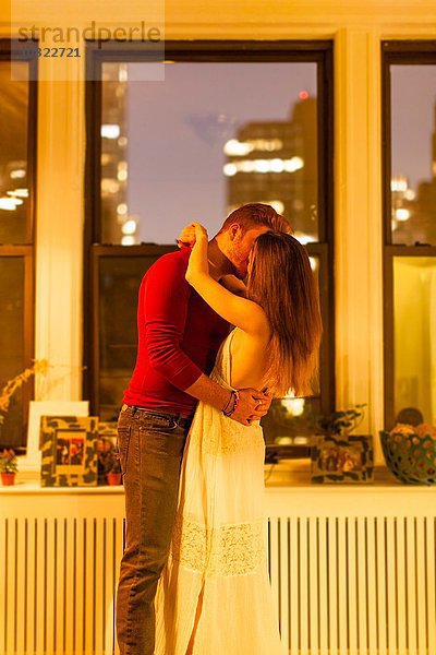 Seitenansicht des Paares in der Wohnung stehend küssend
