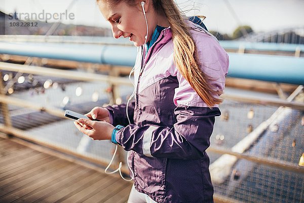 Mittlere erwachsene Läuferin wählt Smartphone-Musik auf der Fußgängerbrücke