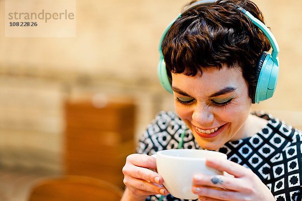 Mittlere erwachsene Frau  Kopfhörer tragend  Kaffeetasse haltend  lächelnd