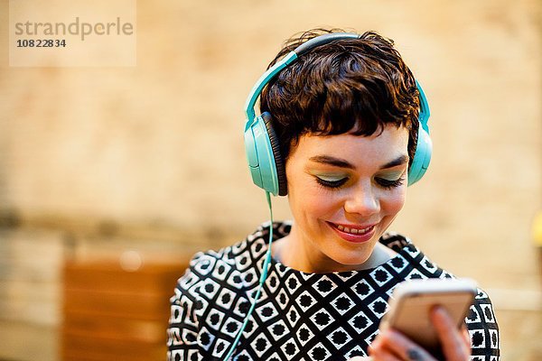 Mittlere erwachsene Frau  Kopfhörer tragend  Smartphone betrachtend  lächelnd