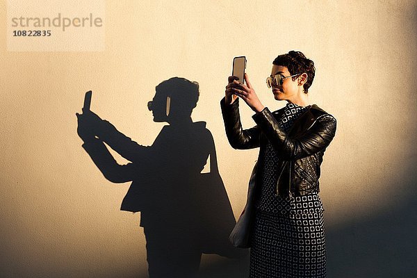 Mittlere erwachsene Frau beim Selbstporträt  mit Smartphone  Schattenwurf an der Wand neben ihr