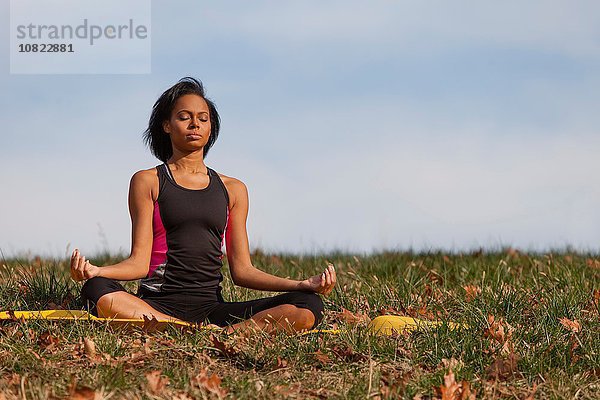 Junge Frau auf Yogamatte sitzend  im Freien  in Lotusstellung