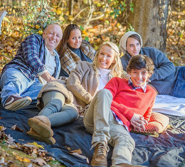 Porträt eines reifen Paares mit Jugendlichen und erwachsenen Kindern  die sich auf einer Picknickdecke im Wald entspannen.