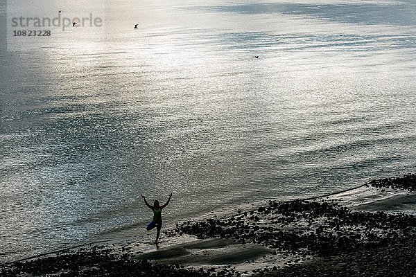 Hochwinklige Silhouette einer jungen Frau  die Yoga praktiziert  stehende Baumhaltung am Strand