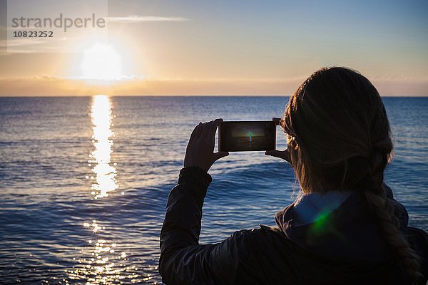 Über der Schulter Silhouette einer jungen Frau  die den Sonnenuntergang über dem Meer fotografiert  Villasimius  Sardinien  Italien