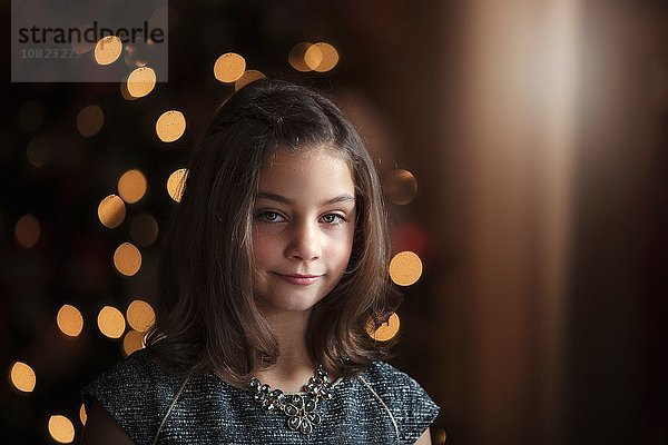 Porträt eines Mädchens vor dem Weihnachtsbaum mit lächelndem Blick auf die Kamera