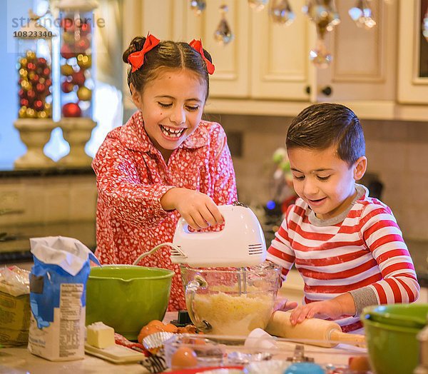 Kinder in der Küche im Pyjama mit Handmixer auf Keksteig lächelnd