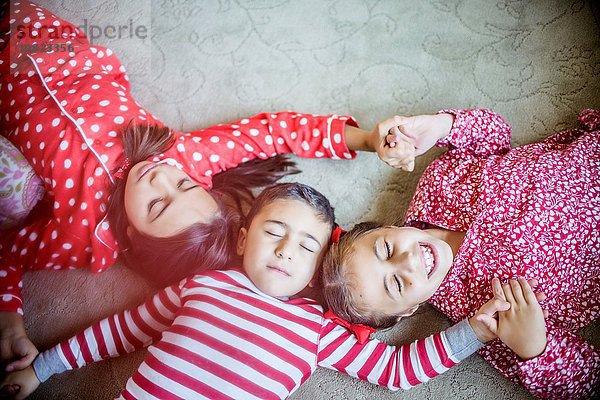 Draufsicht auf Kinder im Pyjama  die auf einem Teppich liegen und die Augen geschlossen halten.