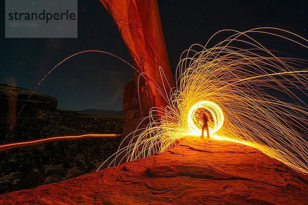 Silhouette einer Person  die nachts gelbe  kreisförmige Lichtspuren auf einer Felsformation erzeugt  Utah  USA